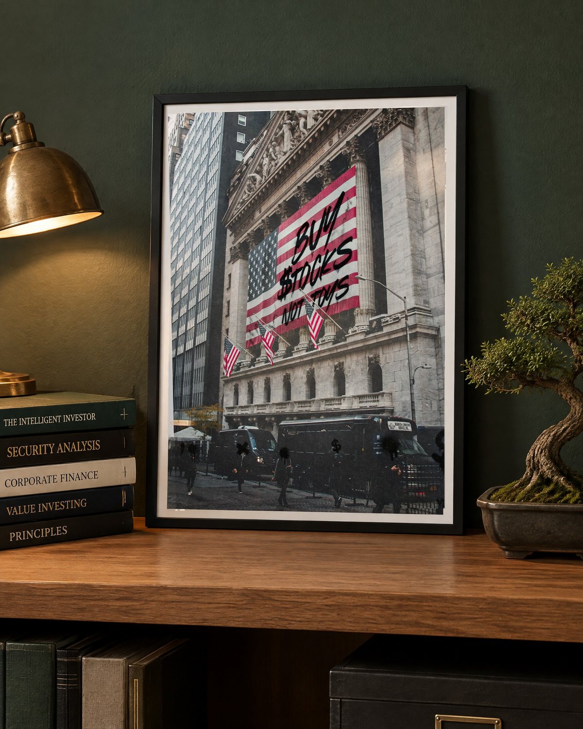 Das gerahmte Poster an eine dunkelgrüne Wand gelehnt, daneben Bücher, eine Messinglampe und ein Bonsai